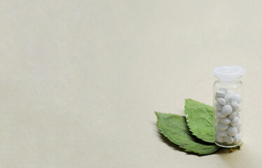 Transparent bottle with white pills and two leaves from wood on craft background