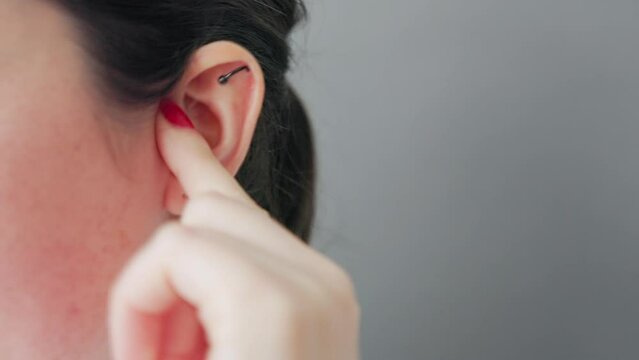 Close-up of the face of a young Caucasian woman scratching and rubbing her ear with an earring and piercing. Concept of earache and deafness.
