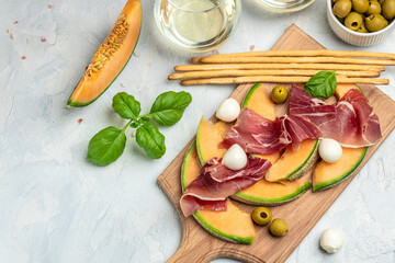 mediterranean salad with prosciutto or jamon, mozzarella and green basil leaves and Cantaloupe melon on white table, traditional Spanish and Italian appetizer served with wholemeal grissini, top view