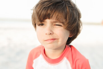 little boy with sand in his eye winking 
