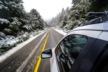 carro viajando en camino de asfalto bajo tormenta de nieve con pinos nevados en bariloche argentina ruta