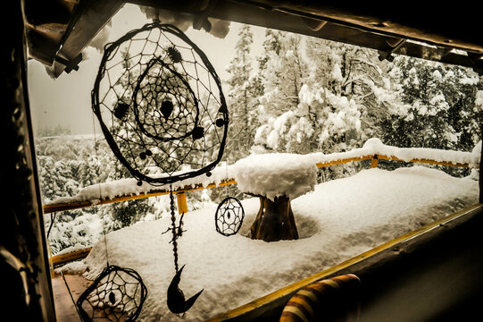 vista de paisaje desde ventana de caba&ntilde;a balconcon mesa redonda de madera y baranda nevado con pinos de fondo
