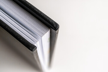 detalle de esquina de libreta negra cerrada con hojas blancas sobre fondo blanco