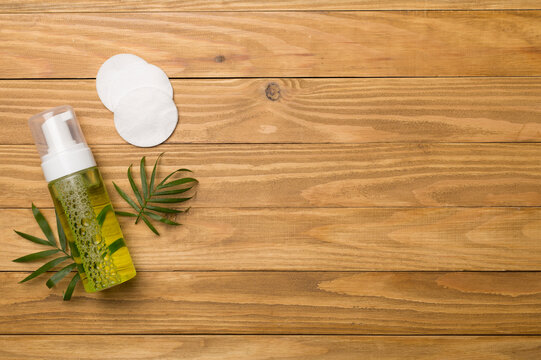Foaming facial cleanser and cotton pads on wooden background, top view
