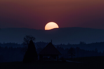 Obraz premium Sunset behind swiss jura mountains, with silhouette of a house in foreground