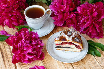 Floral tea time with piece of fresh baked berry pie, cup of tea and lush dark pink peony flowers. Morning breakfast with fresh pastry and floral tea. Flat lay, top view.