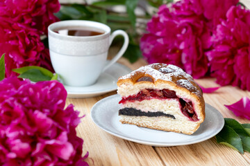 American pie on plate on rustic wooden board with cup of tea and lush deep pink peonies on background. Easy recipe of cherry cake, vegan dessert gluten free. Homemade bakery with flaky crust.