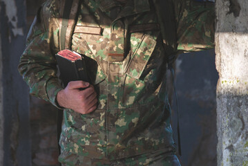 Soldier dressed in camouflage uniform holding a bible in his hand. Soldier reading and meditating on God's word - 494761407