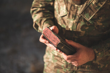 Soldier dressed in camouflage uniform holding a bible in his hand. Soldier reading and meditating on God's word