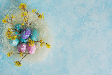 Easter painted eggs still life aesthetics. Festive Easter composition. Flat lay of the nest, blue, pink, purple eggs, flowering branches on a gray background. Happy Easter, greeting card. Copy space
