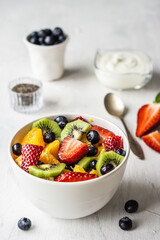 Fresh organic fruit salad with strawberries orange kiwi in white bowl on a gray background