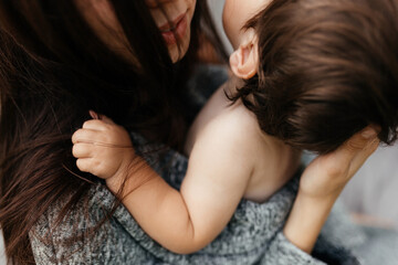 Naklejka premium Beautiful brunette mother plays with her son outdoors on a gray background in summer, the son holds his mother by the hair. Close-up