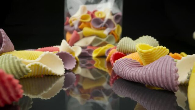 Creative multicolored pasta farfalle on a black background in perspective with packaging in background. Moving extreme macro