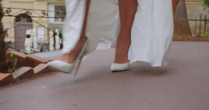 beautiful female legs in white shoes and a white dress with a high slit are walking along the city streets against a blurred background of people that I shoot on the phone. close-up
