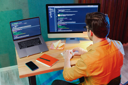 Top back view from above professional young software engineer IT specialist programmer man in shirt work at home writing code on laptop pc desktop computer typing script. Program development concept.