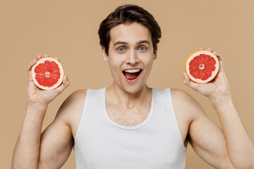 Attractive excited amazed young man 20s perfect skin in undershirt hold in hand half of grapefruit...