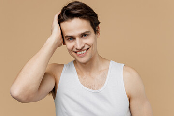 Attractive smiling fun young man 20s perfect skin in undershirt look camera touch strong black hair isolated on pastel pastel beige background studio. Skin care healthcare cosmetic procedures concept.