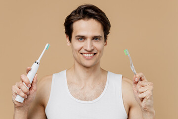 Attractive smiling fun young man 20s perfect skin in undershirt hold choice electric brushes choose...