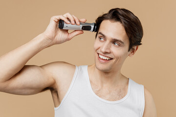 Attractive young man 20s perfect skin in undershirt hold electric razor grooming with trimmer look...