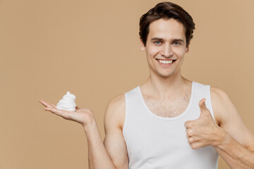 Attractive young man 20s perfect skin in undershirt hold in hand arm palm shaving foam show thumb...