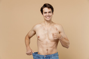 Satisfied young man 20s with naked torso show loose pants show thumb up isolated on pastel pastel...