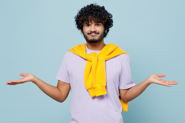 Surprised young bearded Indian man 20s years old wears white t-shirt spreading hands shrugging shoulders standing questioned and unaware isolated on plain pastel light blue background studio portrait.