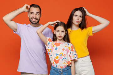 Fototapeta na wymiar Young puzzled thoughtful parents mom dad with child kid daughter teen girl in basic t-shirts scratch hold head isolated on yellow background studio portrait. Family day parenthood childhood concept