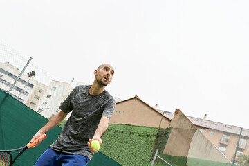 Young man with grey t-shirt and tennis ball in hand right before throw to serve during match