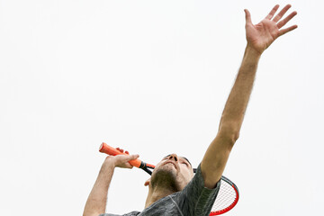 Young tennis player with grey t-shirt about to hit serve with racket over white background