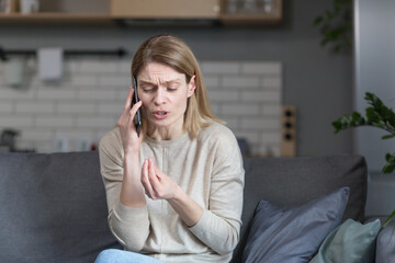 Annoyed woman at home sitting on the couch and talking on the phone