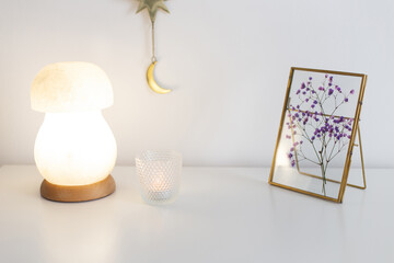 Golden photo frame with purple gypsophyla flowers, night salt lamp and candle on white table. 