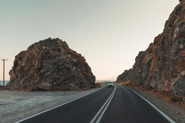 Asphalt road going between rocks during a sunset in Rhodes, Greece