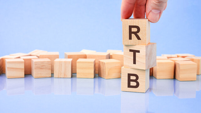 close up image hand of a young businessman holding a wooden cube with letter R. RTB on wooden cube on a blue background with copy space