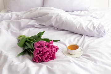 Obraz na płótnie Canvas Bouquet of pink tulips and cup of tea on bed with lilac linen.