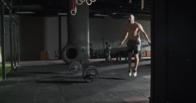 Shirtless sportsman jumping rope during training in gym