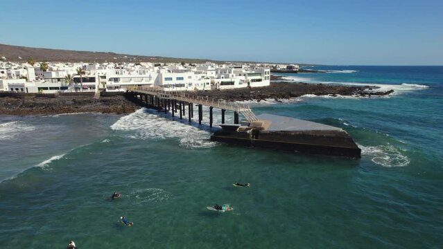 Aerial shot, surfers training surfing on the La Garita beach in Arrieta small coastal spanish village, famous place among locals and tourists, Lanzarote island. Canary, Spain. Travel concept 
