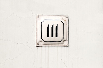 Arabic figure 111 or three in roman numerals painted with black on an old-fashioned square plate on a white wall