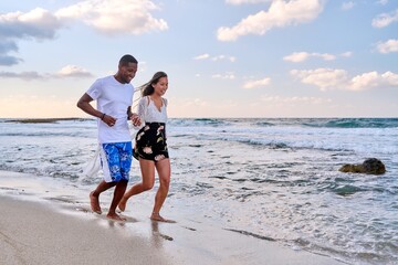 Young happy couple walking on the beach holding hands, copy space