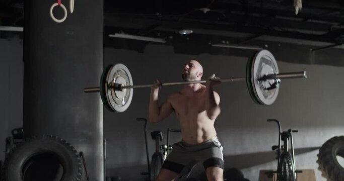 Athletic man doing clean and jerk exercise barbell in gym