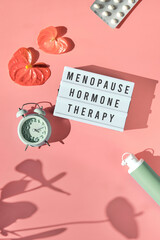 Text Menopause Hormone Therapy, pink frame in hand. Menopause, hormone therapy concept. Estrogen replacement therapy awareness design. Pink background with exotic leaves, flowers, pills, estrogene gel - obrazy, fototapety, plakaty