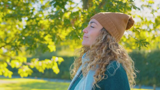 Calm young woman wearing hat and scarf relaxing and breathing in deeply in autumn park - shot in slow motion 