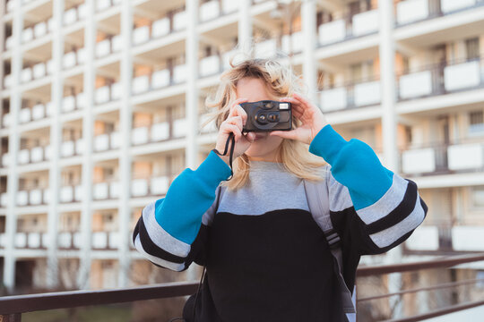 Creative caucasian blonde-haired hipster photographer taking photos of the city with old analog camera. 90s-inspired. High quality photo