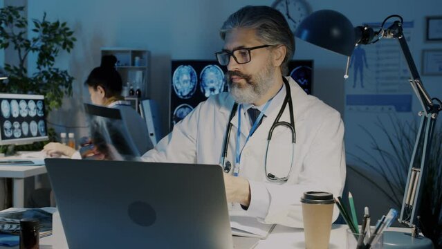 Doctors in uniform studying lungs x-ray images and using computers working in hospital at night during covid-19 pandemic. Medicine and corona virus concept.