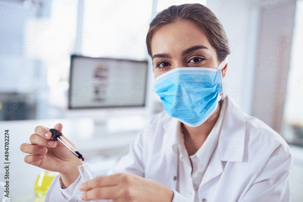 Aufkleber Time for some testing. Portrait of a confident young female scientist wearing a surgical mask while doing a experiment and looking at the camera inside a laboratory.