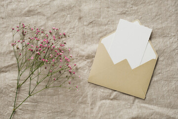 Envelope with blank paper card inside and gypsophila flowers on linen tablecloth. Romantic, love...