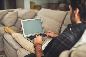 This is how I keep up with the world. Shot of a handsome young man using his laptop while relaxing on a couch at home.