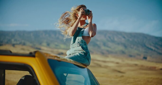 Beautiful young woman taking photographs on summer road trip, hair blowing in the wind in slow motion, travel and adventure nomadic lifestyle