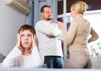 Obraz premium Upset tired son suffering from mom and dad arguing at home