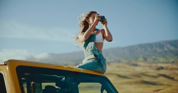 Beautiful young woman taking photographs on summer road trip, hair blowing in the wind in slow motion, travel and adventure nomadic lifestyle