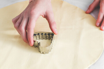 The hand of a caucasian teenage girl cuts out a shortbread dough with a metal cookie cutter on a white parchment.